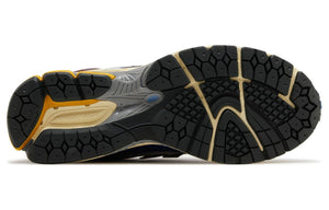 Bottom outsole view of white, blue, and purple New Balance shoes 1906R model, featuring black rubber traction tread, cream flex grooves, yellow heel accents, and a grey midfoot Stability Web arch support shank.