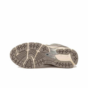 Bottom view of cream and silver New Balance shoes, showing the textured grey rubber outsole, diamond-patterned tread, and midfoot Stability Web support structure