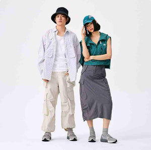 Male and female models stand side-by-side, each wearing a distinct outfit with the New Balance 1906L Grey sneakers, perfectly illustrating how the shoe serves new balance 1906l men and women (نيو بالانس 1906L رمادي للنساء والرجال).