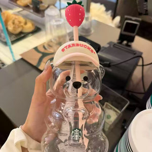 A close-up view of the Starbucks bear cup 2026 pink edition, featuring a clear glass bear-shaped tumbler with a pink Starbucks cap and a strawberry-topped straw.