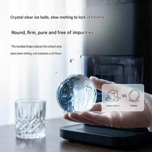Close up of a person holding a perfectly transparent, pure ice sphere made by a crystal ice maker machine next to a glass.