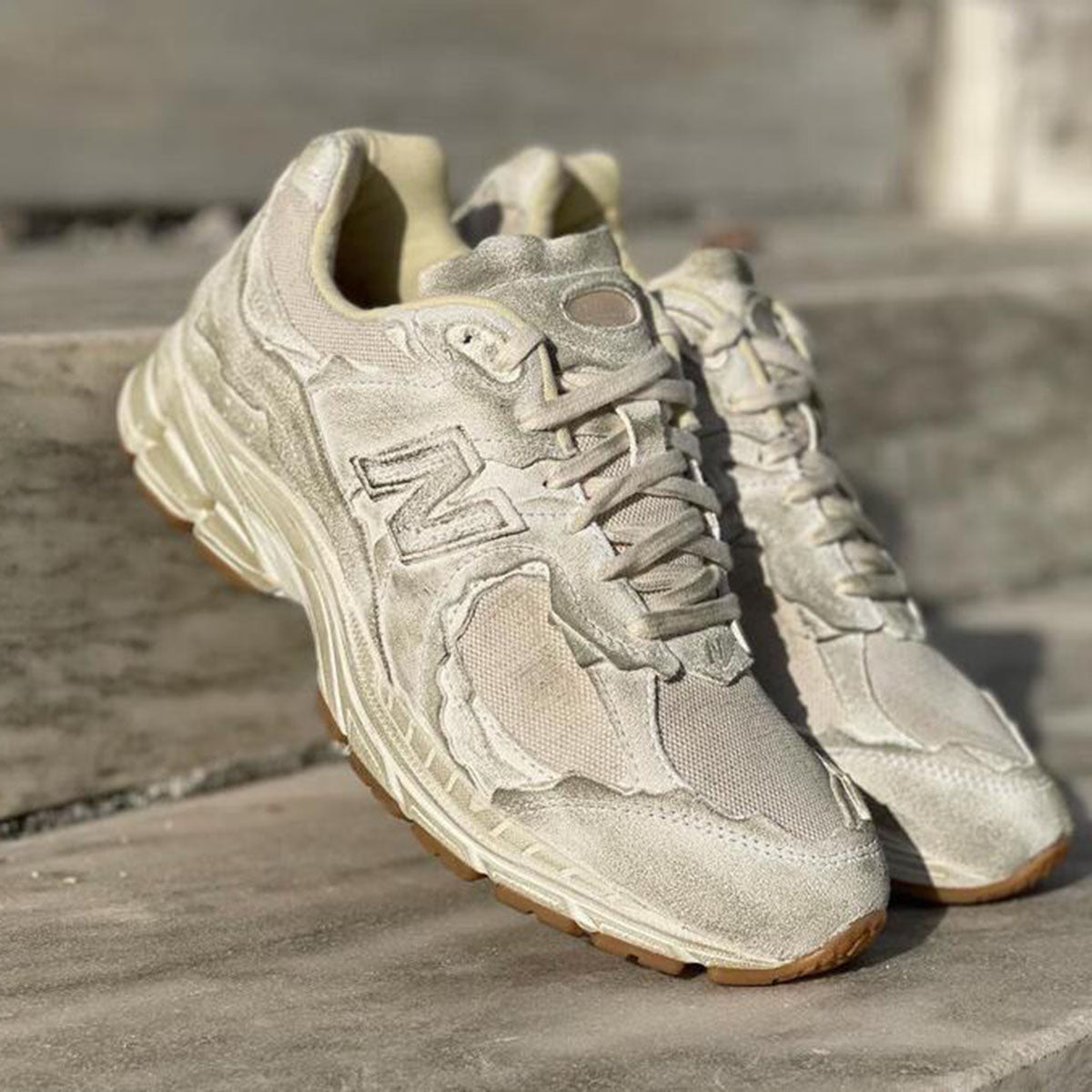 حذاء New Balance 1906R بلون بيج بتصميم فني غير تقليدي، بمواد خشنة ومظهر متآكل متعمد.