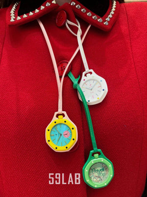 A white and a green Audemars Piguet x Swatch Royal Pop pocket watch worn as stylish neck pendants over a red top.