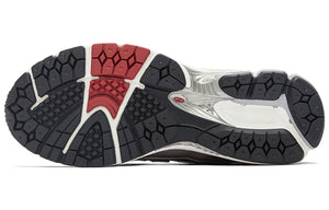 Bottom outsole view of white, silver, and red New Balance shoes 1906R model, featuring a black rubber tread pattern with red forefoot traction accents, off-white heel pods, and a silver midfoot Stability Web arch support shank.