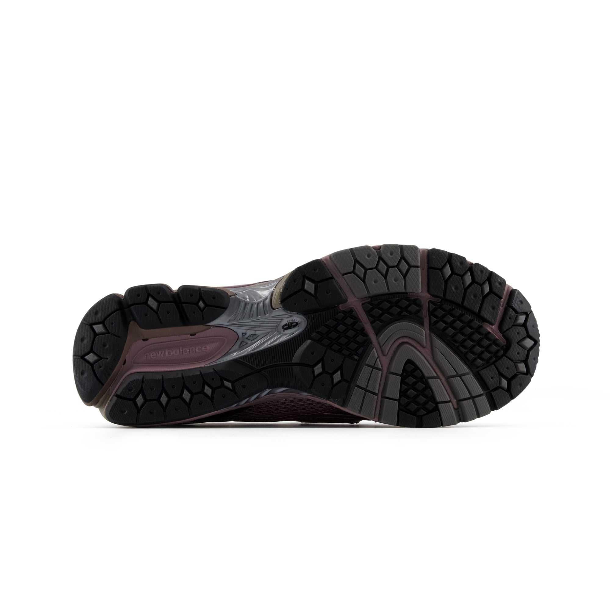 Bottom view of a New Balance shoe displaying the complex black and dark grey rubber outsole, featuring textured traction pods and a supportive midfoot bridge for grip