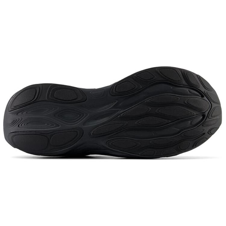 Bottom view of an all-black New Balance running shoe, displaying the full rubber outsole with textured, wave-like traction patterns and flex grooves