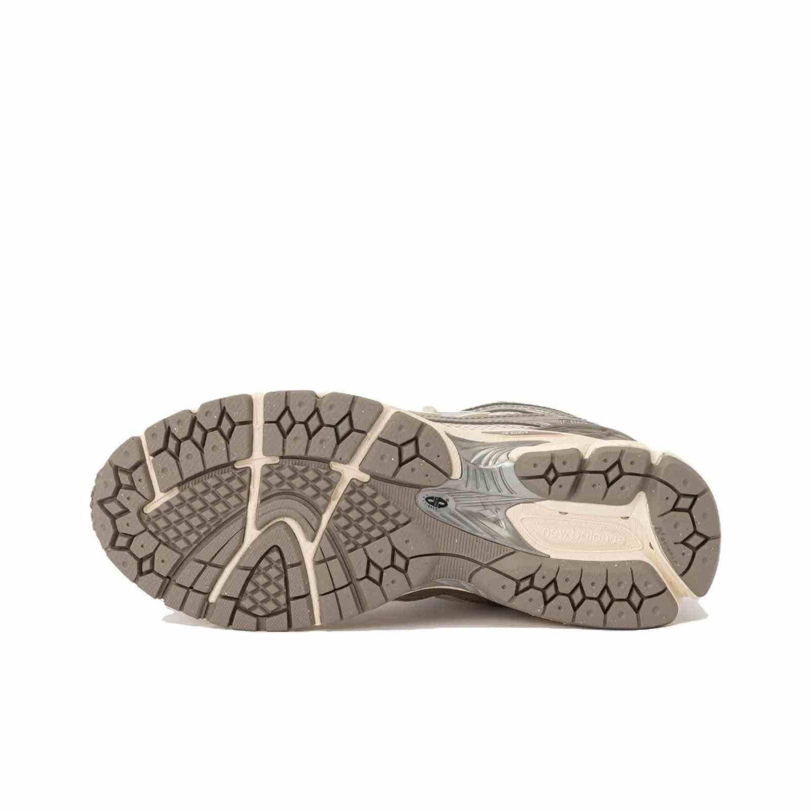 Bottom view of cream and silver New Balance shoes, showing the textured grey rubber outsole, diamond-patterned tread, and midfoot Stability Web support structure