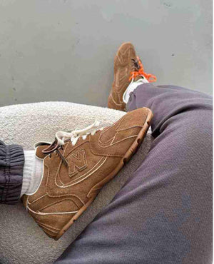 First-person view of brown suede New Balance x Miu Miu shoes worn with grey sweatpants.