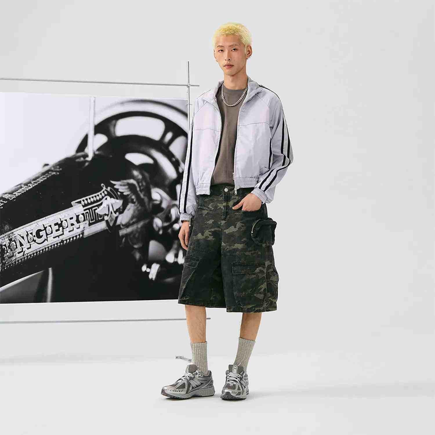 Full-length studio view of a model styled in dark grey and metallic silver New Balance running shoes.