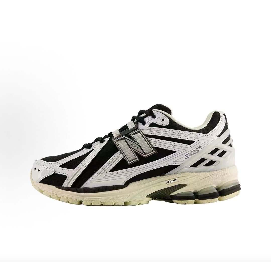 Lateral side profile of monochromatic New Balance shoes 1906R model, featuring a black mesh upper, metallic silver and white leather overlays, metallic "N" logo, and a cream-colored N-ergy cushioned sole.