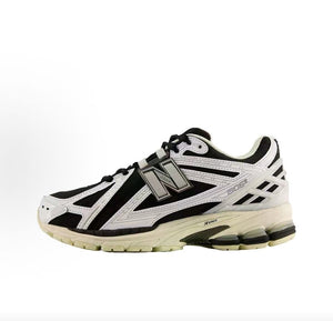 Lateral side profile of monochromatic New Balance shoes 1906R model, featuring a black mesh upper, metallic silver and white leather overlays, metallic "N" logo, and a cream-colored N-ergy cushioned sole.