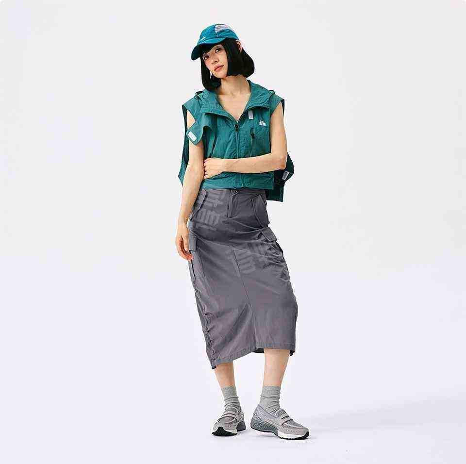 A full-body view of a female model styling the New Balance 1906L grey loafer with a modern, oversized green shirt and grey skirt. Showcases the versatile fashion-forward look of new balance 1906l women (نيو بالانس 1906L رمادي للنساء والرجال).