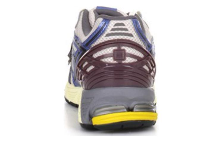 Rear heel view of white, blue, and purple New Balance shoes 1906R model, featuring a deep purple molded TPU heel cage, white mesh collar, metallic blue trim, and a grey N-ergy cushioned midsole with yellow heel pods.