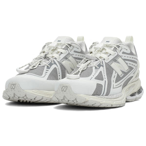 Three-quarter profile shot of a pair of grey and white New Balance shoes 1906R model, featuring grey textured mesh uppers, white and silver overlays, white toggle speed lacing system, heel pull tabs, and white N-ergy cushioned midsoles with silver heel pods.