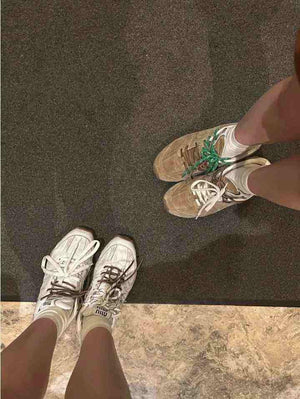 Top-down perspective of two people wearing brown suede and off-white New Balance x Miu Miu shoes.